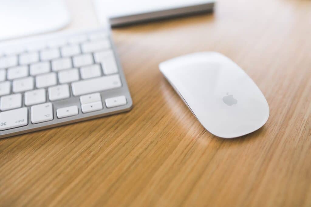 Clavier Bluetooth blanc et souris Apple blanches posés sur un bureau en bois clair.