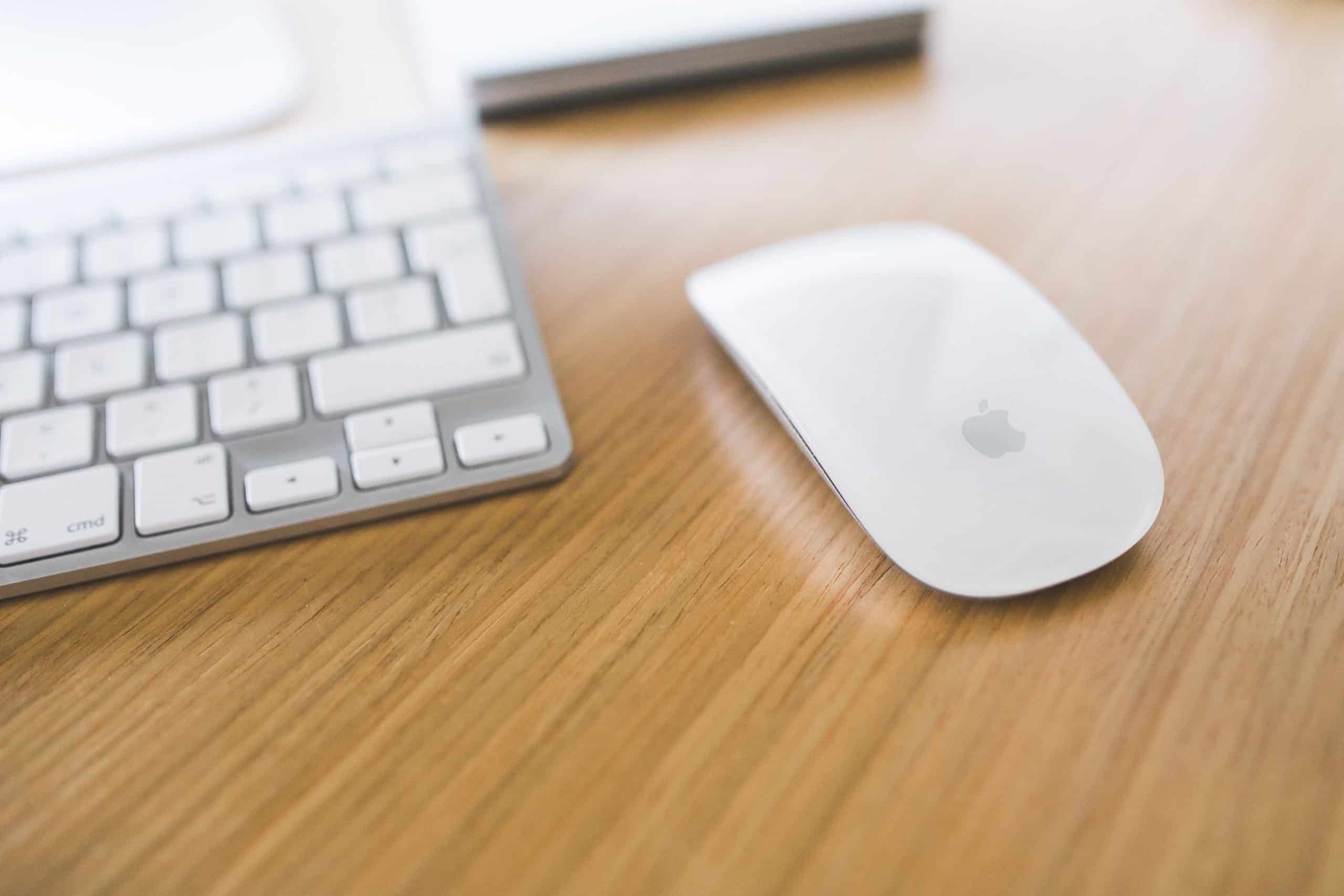 Clavier Bluetooth blanc et souris Apple blanches posés sur un bureau en bois clair.