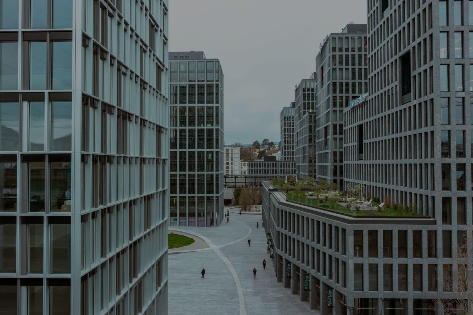 Allée piétonne large à Lancy Pont-Rouge entre immeubles modernes en verre et béton sous ciel couvert, avec quelques passants, illustrant le service de dépannage informatique local