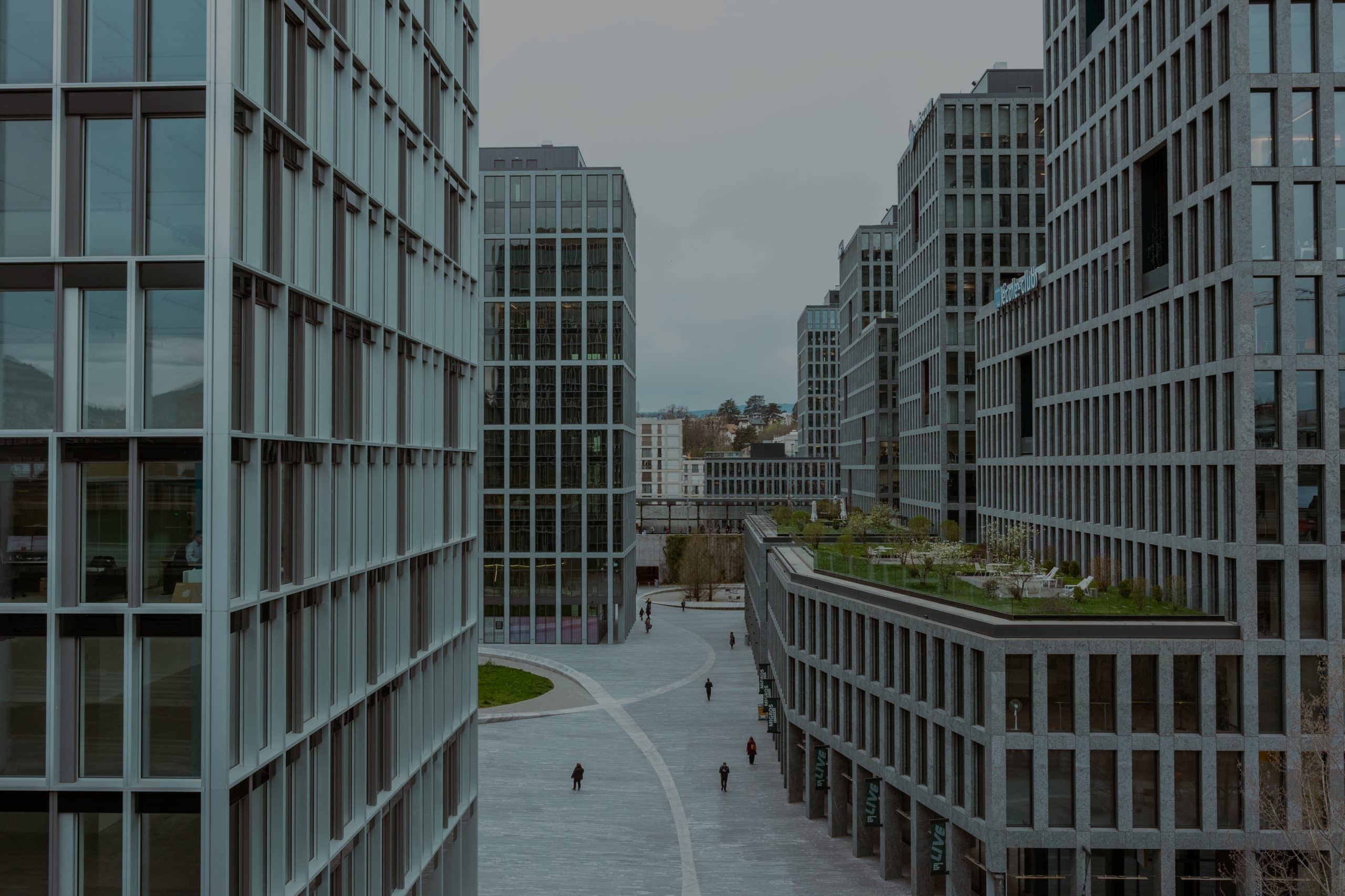 Immeubles de bureaux modernes en verre et béton avec large allée piétonne et toit-terrasse végétalisé.