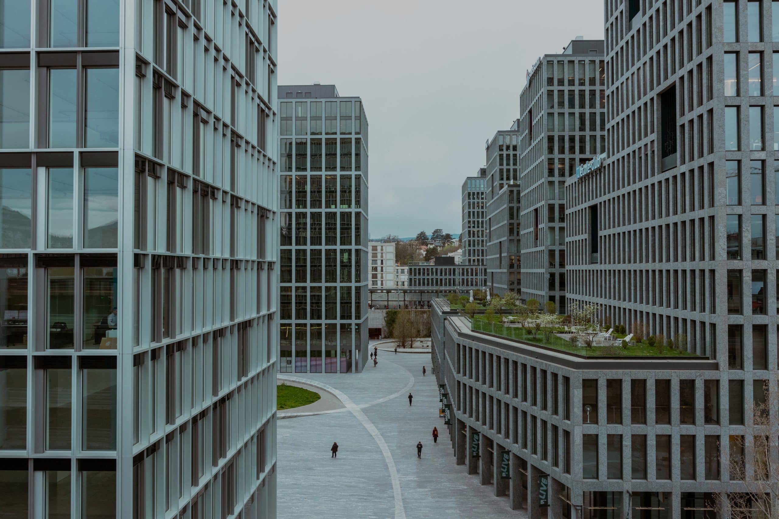 Espace urbain moderne avec allée piétonne et terrasse végétalisée - Dépannage Informatique Genève Espace urbain avec immeubles de bureaux modernes, allée piétonne et terrasse végétalisée.