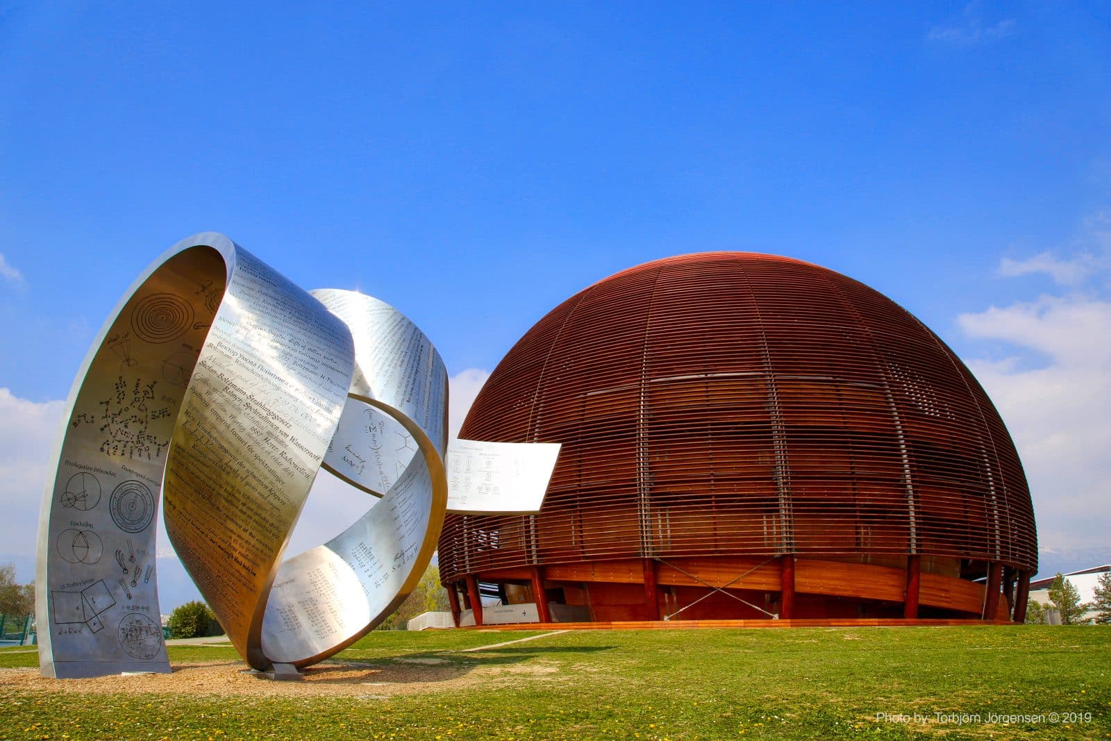 Dôme en bois du CERN à Meyrin avec pelouse et sculpture métallique en forme de ruban infini gravée, illustrant le service de dépannage informatique local