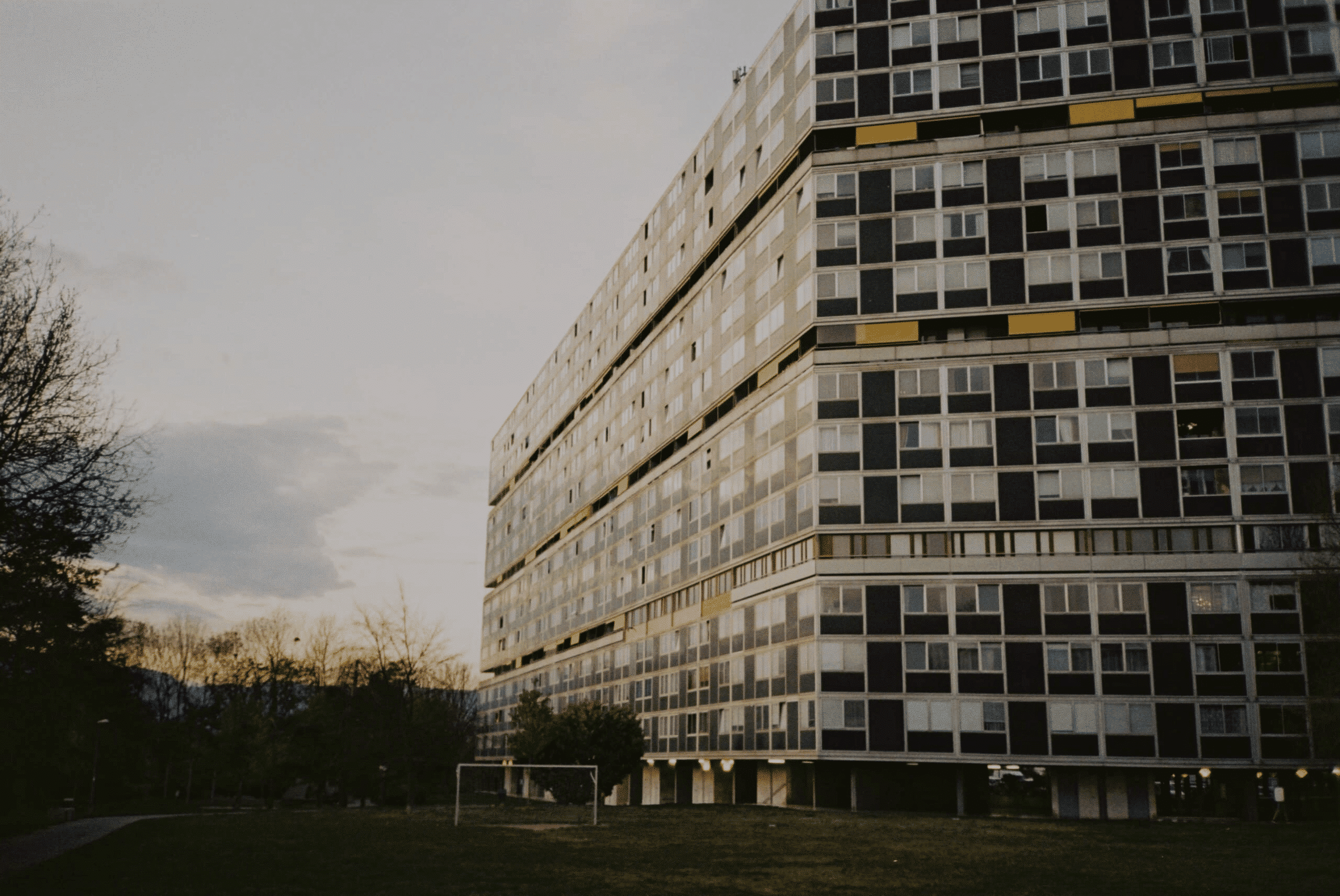 Immeuble résidentiel à plusieurs étages avec nombreuses fenêtres, proche d'un terrain de football.